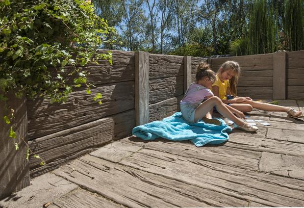 Kinder sitzen im Garten vor Palisaden in Holzoptik